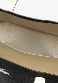 Borsa a tote in pelle nero con dettagli bianchi, chiusura con zip e interno beige testurizzato, con un piccolo logo sulla parte esterna.