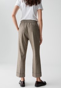 Bruine geruite broek van een gestructureerde stof, met een elastische tailleband, omgeslagen broekspijpen en zijzakken. Gepaard met een witte shirts met korte mouwen.