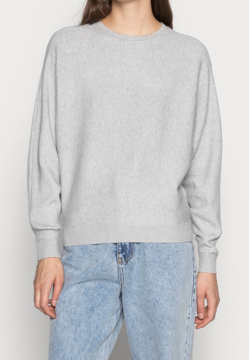 Pull léger gris avec un col rond, des épaules tombantes et des poignets côtelés, associé à un jean denim bleu clair.