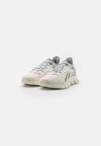 Lightweight running shoes with a textured cream upper, grey accents, and a thick, cushioned sole. Features lacing and logo detail.