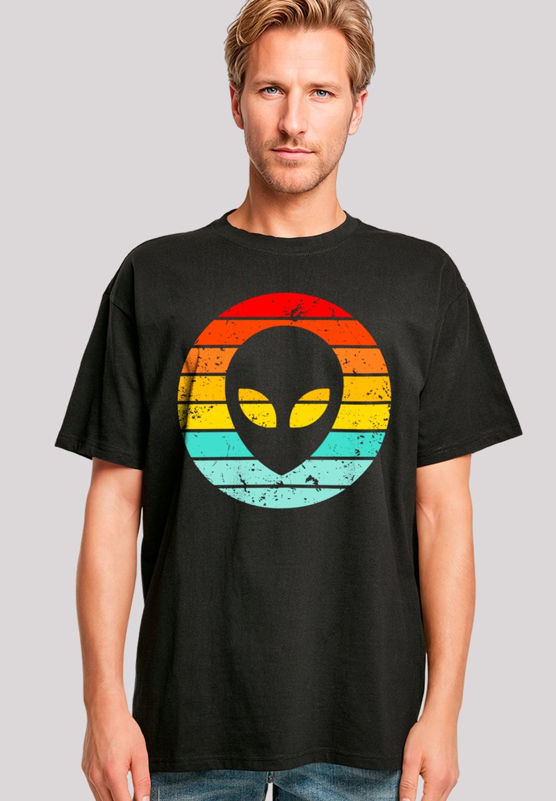 Schwarzes T-Shirt mit einem verwitterten Grafikdesign eines Alienkopfes und konzentrischen Streifen in Rot, Orange und Türkis. Lässiger Schnitt, kurze Ärmel.