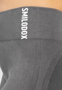 Szare legginsy z żeberkowym pasem w białym kolorze z napisem "SMILODOX". Charakteryzują się teksturowanym materiałem oraz dopasowanym krojem z bezszwowymi detalami.