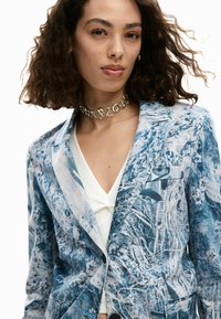 Blazer blu a motivo con tessuto strutturato, con rever a incavo, chiusura con un solo bottone e dettagli floreali su tutta la superficie.