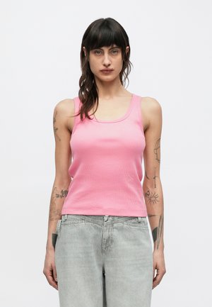 Ροζ τοπ με ριπ υφή, στρογγυλή λαιμόκοψη και λεπτές τιράντες. Φοριέται με ανοιχτό γκρι τζιν παντελόνι, με εμφανή τατουάζ στα μπράτσα.