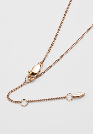 Collier chaîne en or rose avec fermoir mousqueton et petite plaque ovale gravée "FOSSIL" sur un fond clair uni.