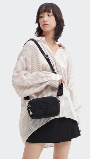 Borsa a spalla nera trapuntata con dettaglio rotondo del logo, dotata di tracolla staccabile e hardware in argento. Il modello indossa una camicia a righe oversize.