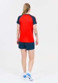 Rød og marineblå sportstrøje med korte ærmer, parret med marineblå shorts. Trøjen har en rund halsudskæring og en glat tekstur.
