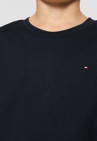 Laivaston sininen puuvillapaita, jossa on pyöreä pääntie ja pieni punavalko-sinisesti brodeerattu logo vasemmassa rinnassa. Pehmeä materiaali.