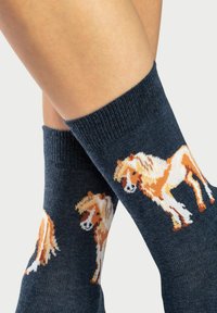 Marineblaue Socken mit gerippter Textur, die ein gemustertes Design von braunen und weißen Pferden in verschiedenen Positionen zeigen.