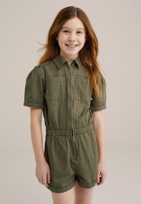 Salopette verde oliva a maniche corte con zip frontale, due tasche sul petto, vita elasticizzata e risvolti. Tessuto morbido.