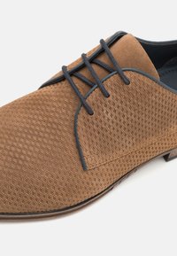 Brązowe, teksturowane buty eleganckie z falistym wzorem, z ciemnoniebieskimi sznurowadłami i wykończeniem, okrągłym noskiem oraz gładką podeszwą.