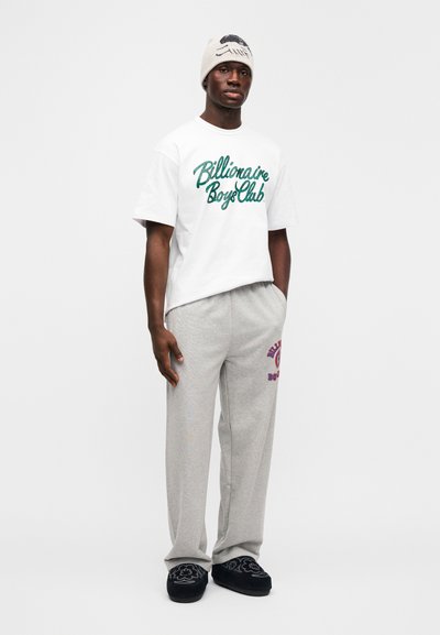 Λευκό βαμβακερό t-shirt με πράσινο λαμπερό λογότυπο, γκρι βαμβακερή φόρμα με κόκκινο κείμενο και μαύρες υφασμάτινες παντόφλες. Απλός σχεδιασμός, άνετη εφαρμογή.