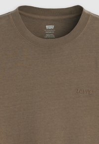 Ruda retro stiliaus prigludusi medvilninė marškinėlė. Su gofruotu apvaliu kaklu ir siuvinėtu "Levi's" logotipu kairėje pusėje.