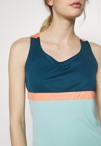 Sportowy top bez rękawów w kolorze naturalnym z koralowymi i jaśniejszymi niebieskimi poziomymi paskami. Gładki, elastyczny materiał z dekoltem w serek.