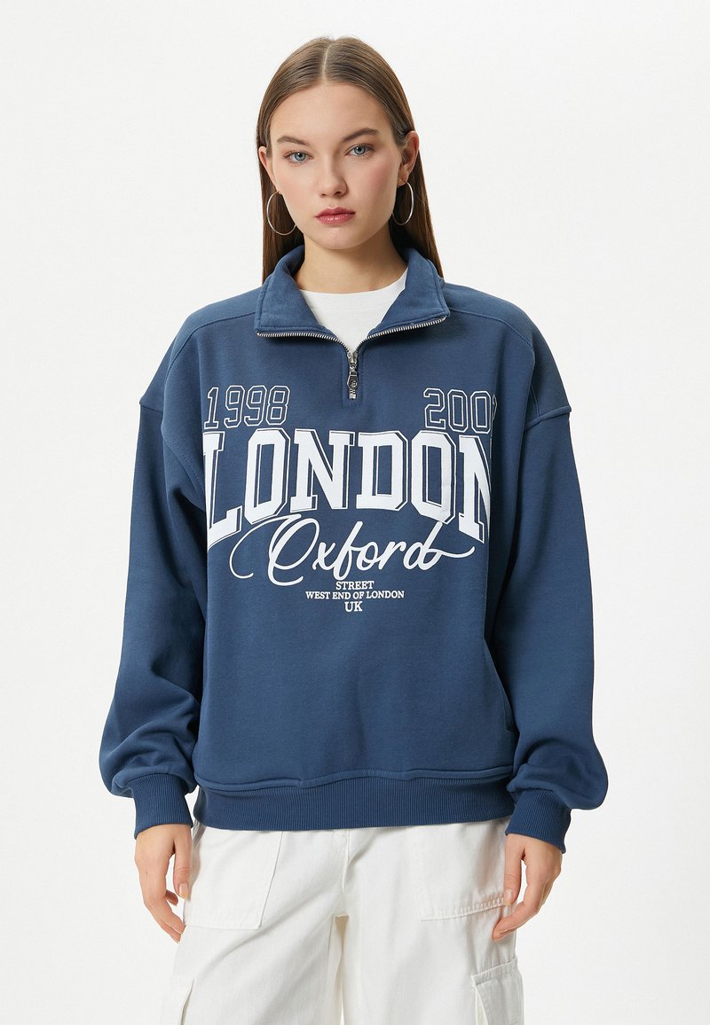 Sudadera de color azul marino con cuello de cremallera de un cuarto, que presenta texto y gráficos en blanco: "LONDRES 1998 2002 Oxford Street West End de Londres Reino Unido."