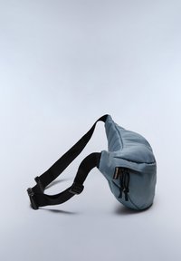 Borsa a spalla morbida blu con design imbottito, tracolla nera regolabile e chiusura a zip. La forma è asimmetrica e compatta.