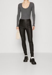 Långärmad, grå topp med rundad halsringning som matchas med tajta svarta fake-läderbyxor. Modellen håller en liten handväska i krämfärg. Tjocka svarta skor.