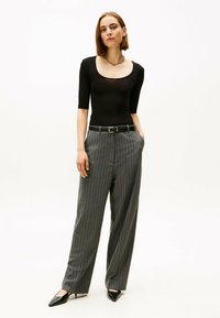 Zwarte bodysuit, grijze pinstripe broek tot de enkel met wide legs, zwarte riem met vierkante gesp, en zwarte pumps met punten.
