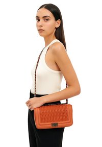 Borsa a tracolla in pelle arancione trapuntata con catena, di forma rettangolare e chiusura metallica. La borsa presenta una superficie texture con un motivo geometrico.