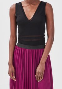 Haut sans manches noir avec un décolleté en V et des panneaux transparents, associé à une jupe plissée magenta et une ceinture noire.