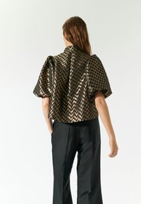 Cropped top a righe chevron in nero metallico e oro, con maniche a sbuffo, abbinato a pantaloni neri su misura. Texture liscia, silhouette strutturata.