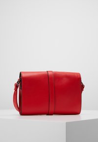 Czerwona skórzana torebka o gładkiej fakturze, prostokątnym kształcie i odpinanym pasku. Posiada poziomy szew i minimalne okucia.