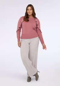 Staubrosa Langarmpullover mit Rüschendetails an den Ärmeln, kombiniert mit hellgrauen, weitgeschnittenen Hosen und olivgrünen Plateau-Stiefeln.