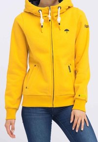 Felpa con cappuccio gialla con zip, realizzata in tessuto di misto cotone. Presenta un cappuccio con coulisse, due tasche laterali e un piccolo logo a forma di ombrello sul petto.