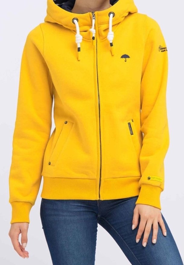 Felpa con cappuccio gialla con zip, realizzata in tessuto di misto cotone. Presenta un cappuccio con coulisse, due tasche laterali e un piccolo logo a forma di ombrello sul petto.