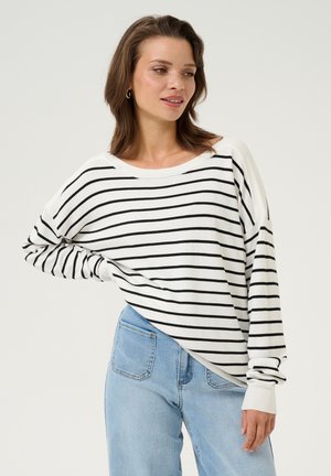White long-sleeve top with black horizontal stripes, featuring a wide neckline, relaxed fit, and ribbed cuffs. Paired with blue denim jeans.