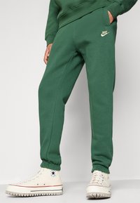 Zelené tepláky se strukturovanou tkaninou, na levé kapse s malým béžovým logem Nike. Doplněné béžovými vysokými teniskami.