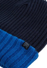 Stickad beanie med en marinblå kropp och en kontrasterande blå ribbad mudd, samt en liten svart logotagg på sidan.