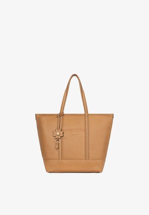 Beige leren tote tas met dubbele schouderriemen en een bloemvormige sleutelhanger die aan de voorste linker riem hangt.