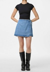 Denim inkningskjol i ljusblått, midjehöjd, med ett knytväskedetalj och kontrasterande söm, kombinerad med en svart t-shirt med kort ärm och knähöga stövlar.