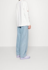 Vit långärmad skjorta med sidoutsparningar, i kombination med ljusblå vida jeans och lavendelplattformsskor.