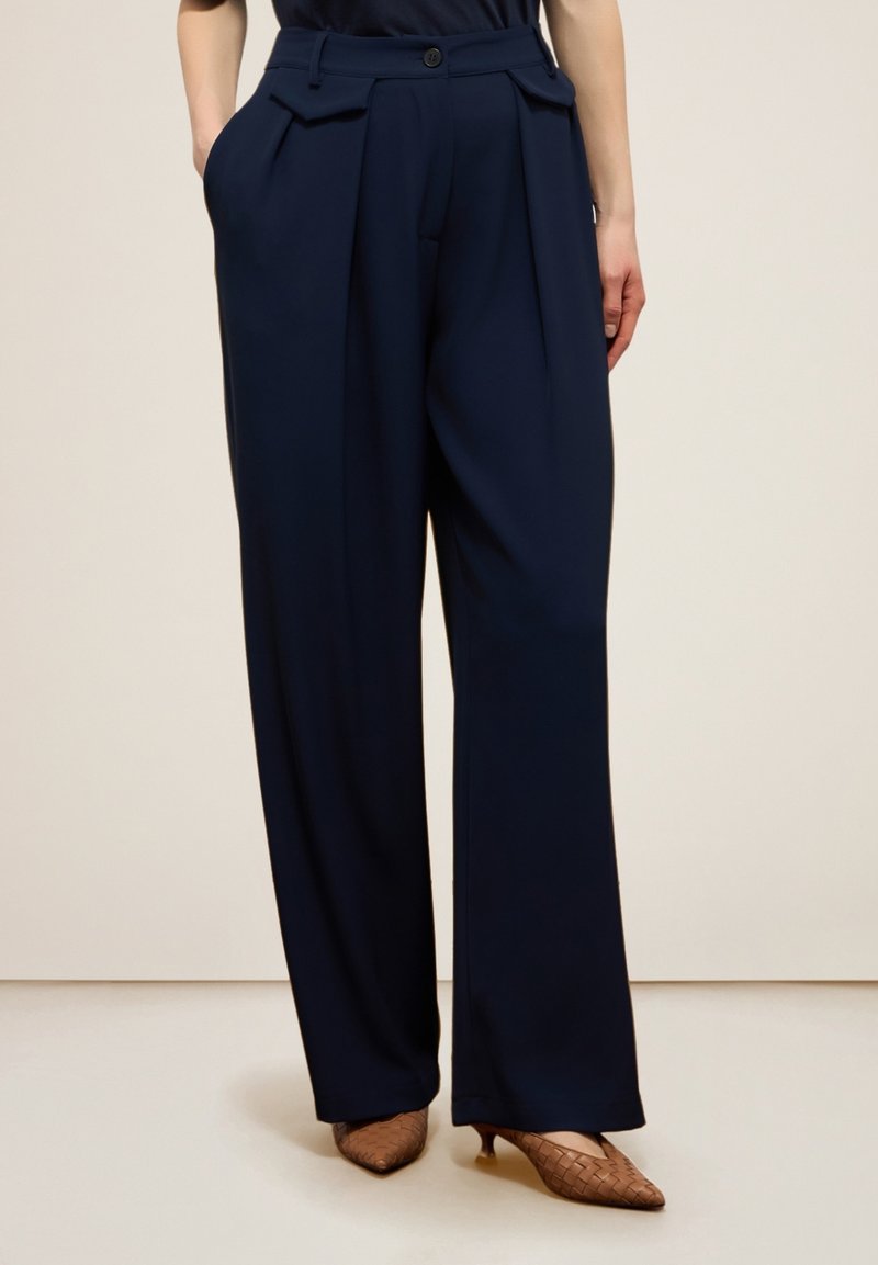 Navyblauwe wijde broek met een hoge taille, voorzien van voorplooien, knoopsluiting en zijzakken. Vloeiend stoffen textuur, gekleed ontwerp.