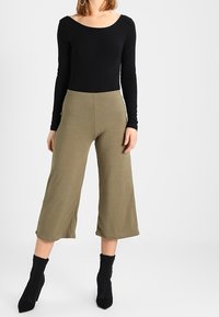 Czarny top z długim rękawem w połączeniu z oliwkowymi, prążkowanymi spodniami typu wide-leg. Czarne botki sięgające kostki uzupełniają stylizację, podkreślając teksturę i proporcje.