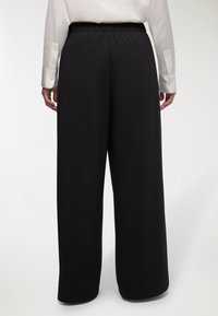 Pantaloni neri a gamba larga con una texture morbida e liscia e una cintura elastica, mostrati da dietro, che evidenziano un design minimalista.
