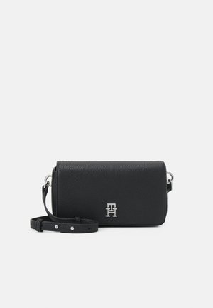 Sac en cuir noir à bandoulière avec une finition texturée, arborant un accent logo argenté, une bandoulière ajustable et un design rectangulaire simple.