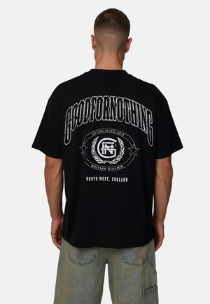 Maglietta nera oversize in cotone con grandi scritte bianche stampate sul retro, con logo circolare e anno di fondazione. Design casual.