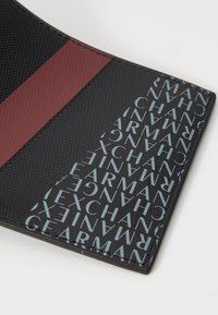 Black wallet featuring a red stripe and textured surface. One side displays repeating text "ARMANI EXCHANGE" in light blue.