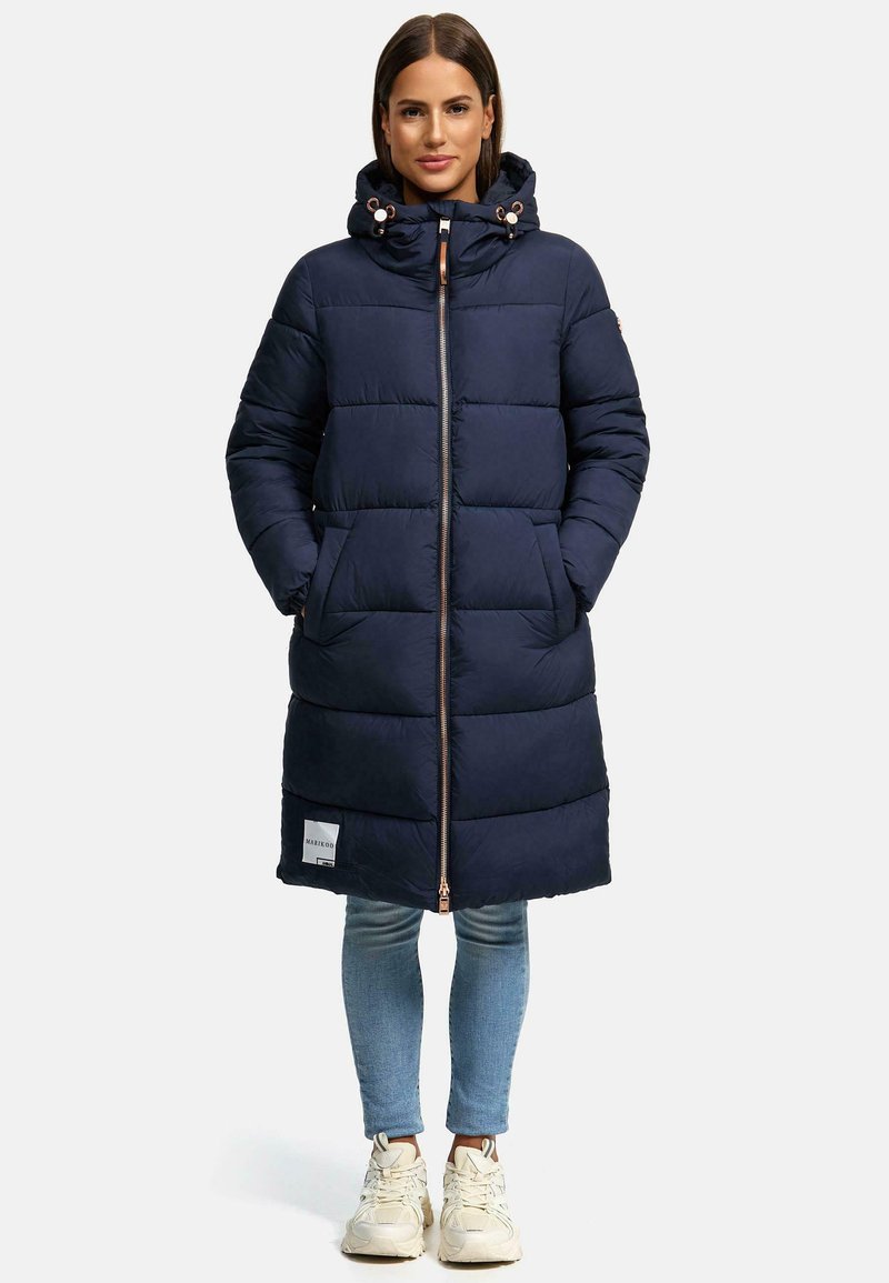 Navy blue puffer coat with a zip closure, hood, and ribbed cuffs. Features side pockets and a logo patch near the hem. Soft, quilted texture.