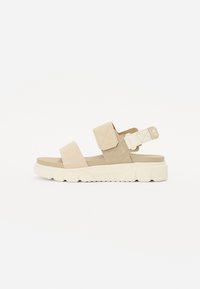 Beige semskede sandaler med to brede stropper og justerbar bakstropp, med en tykk, teksturert hvit gummisåle.