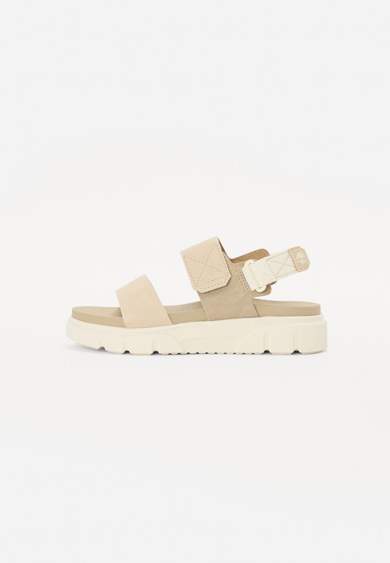 Beige semskede sandaler med to brede stropper og justerbar bakstropp, med en tykk, teksturert hvit gummisåle.