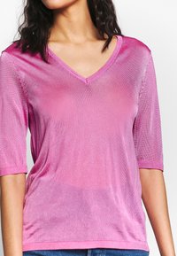 Top rosa a maniche corte con scollatura a V, realizzato in un materiale a coste con una leggera lucentezza e orlo testurizzato a contrasto.