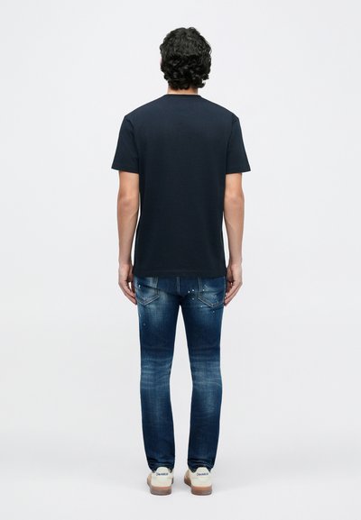 Marineblå t-shirt med korte ærmer kombineret med falmede blå jeans. T-shirten har en rund halsudskæring; jeansene har fem lommer og en afslappet pasform.