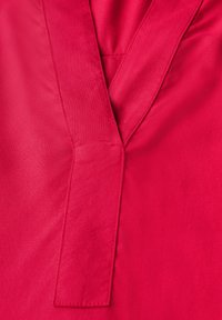 Tissu rouge avec une texture lisse, présentant un design en V et une couture plate et angulaire pour le détail. Aucun motif ni embellissement présent.