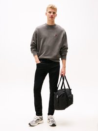 Grijze sweatshirt met klein logo, zwarte slim-fit broek, grijze en witte sneakers, en een zwarte duffeltas met zijvak en ritsen.