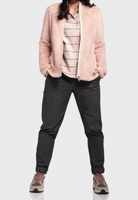 Jasnoróżowa kurtka z sztucznego futra z zamkiem z przodu, zestawiona z koszulą w paski z guzikami, czarnymi spodniami oraz szaro-brązowymi trampkami z burgundowymi akcentami.