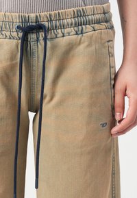 Light beige sweatpants with a drawstring waist, two side pockets, and a subtle logo on the left leg. Soft texture and relaxed fit.